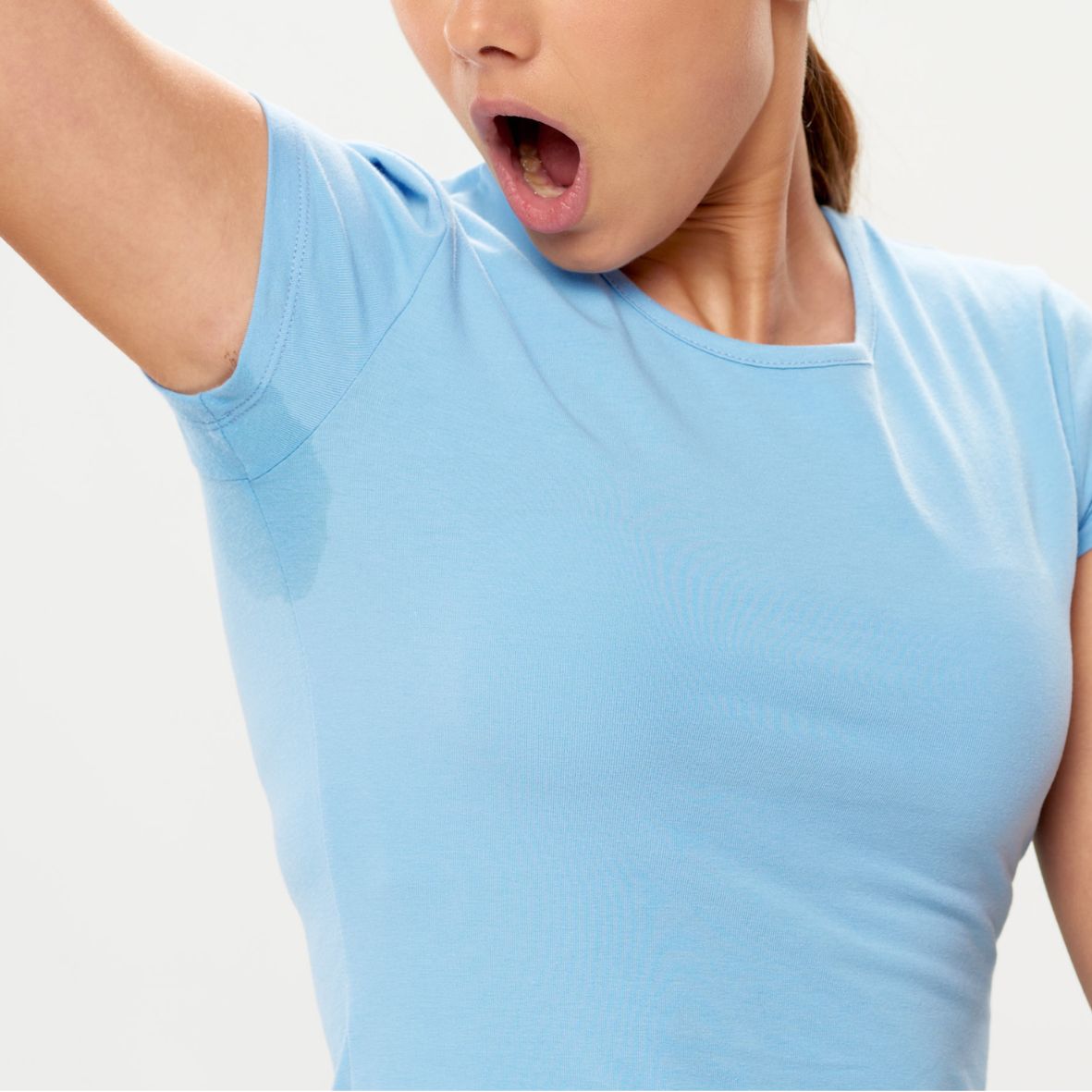 Eine Frau mit angehobenen Arm und Schweißflecken auf dem T-Shirt unter den Achseln